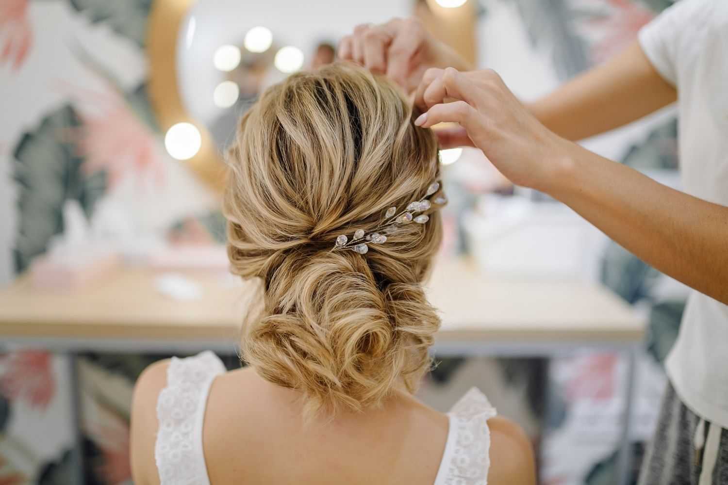 Hairdresser styling a woman's intricate updo with decorative hairpins in a salon.